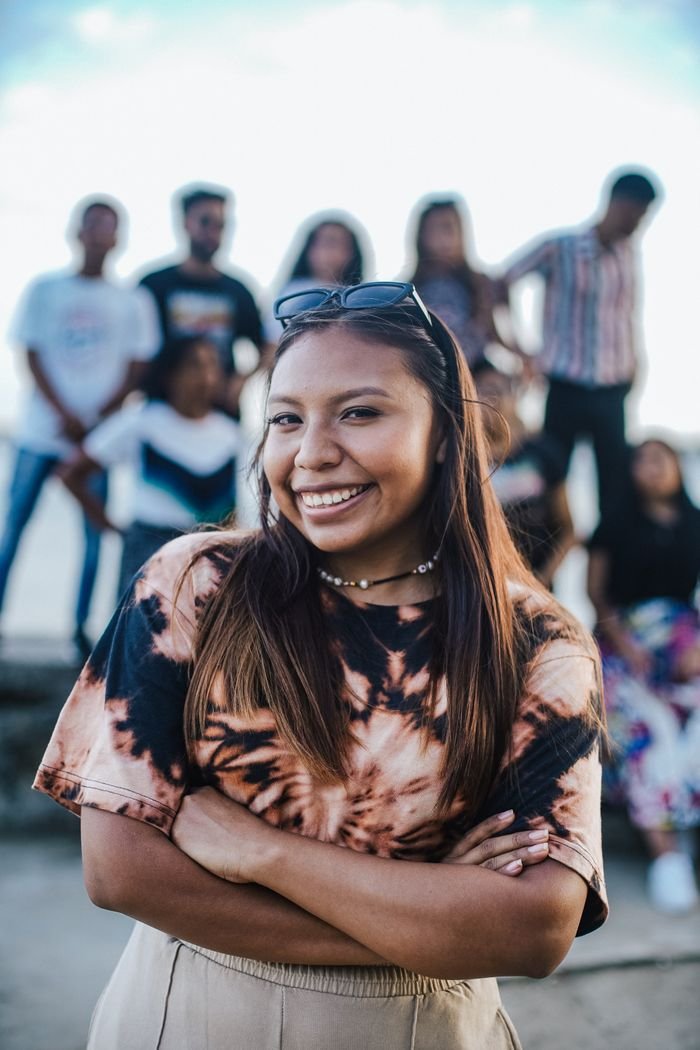 A cheerful woman stands with her arms crossed, surrounded by friends, showcasing happiness and camaraderie.