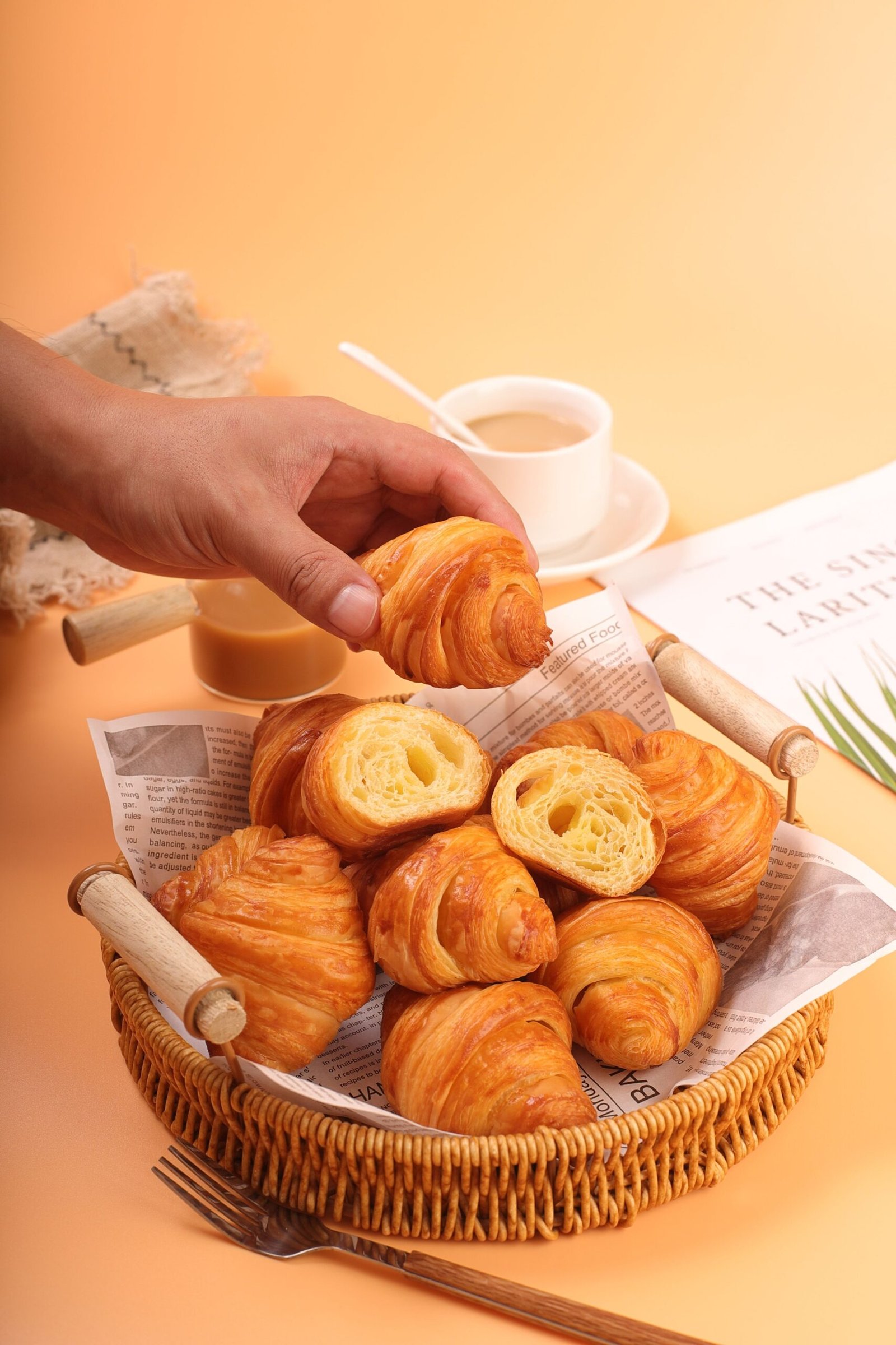 Close-up of freshly baked croissants being picked up from a wicker basket with a warm backdrop.
